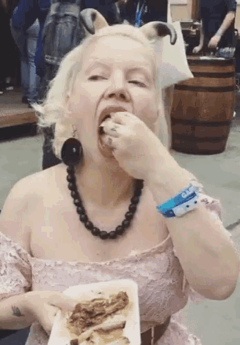 a woman in a pink dress is eating a piece of meat while wearing a wristband that says ' camp '