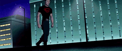 a man in a superman shirt is walking down a sidewalk .