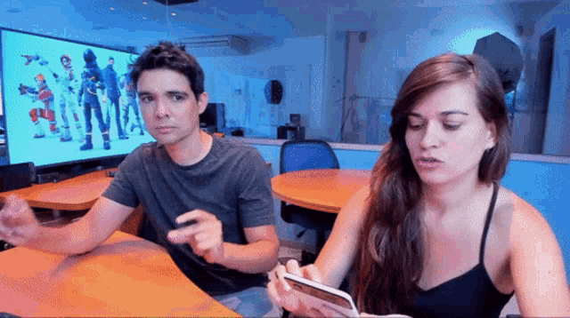 a man and a woman are sitting at a table looking at a phone