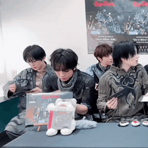 a group of young men are sitting around a table with a poster on the wall that says go in blind