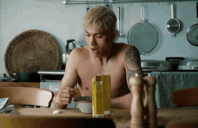 a shirtless man is sitting at a table eating a bowl of food
