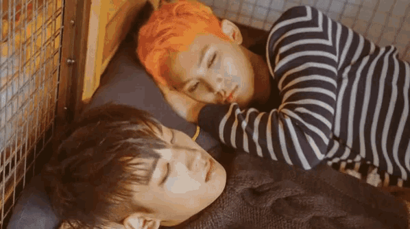 two young men laying on a bed one with orange hair