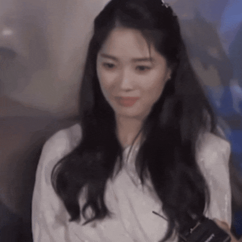 a woman with long black hair is wearing a white shirt and smiling .
