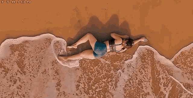 a woman is laying on her stomach in the sand on a beach .