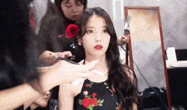 a woman with a red rose in her hair is getting her hair styled