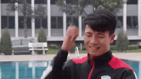 a young man in a red and black jacket is standing in front of a pool .