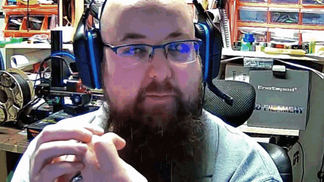 a man wearing glasses and headphones looks at the camera in front of a box that says filament