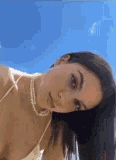 a blurry picture of a woman wearing a pearl necklace and a bikini top
