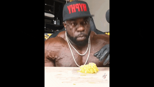 a very muscular man wearing a hat that says yhqyii is eating a piece of food .