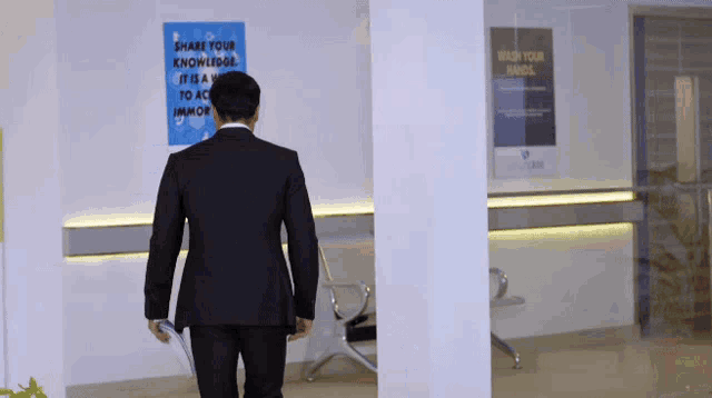 a man in a suit walks in front of a sign that says share your knowledge