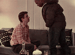 two men are standing next to each other on a couch in a living room .