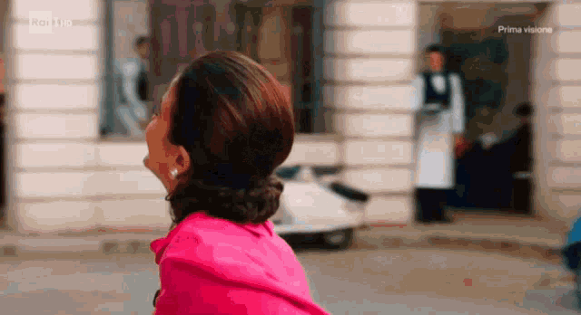 a woman in a pink jacket stands in front of a building