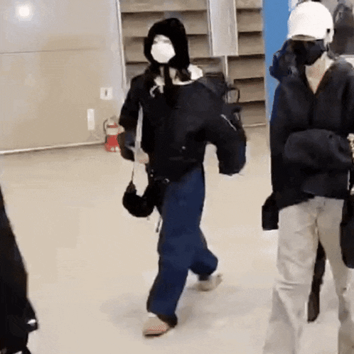 a man wearing a mask and a hood is walking in a room with other people .