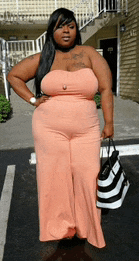a woman in a pink strapless jumpsuit is holding a striped bag