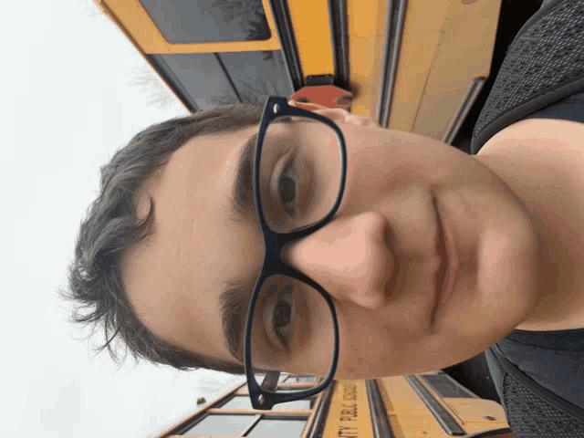 a young man wearing glasses stands in front of a yellow school bus that says city public school
