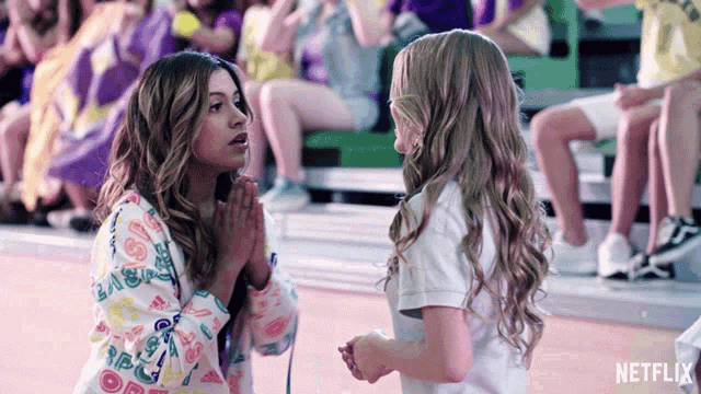 two girls praying in front of a crowd with a netflix logo in the background