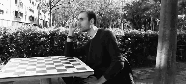 a man sits at a chess board in a park