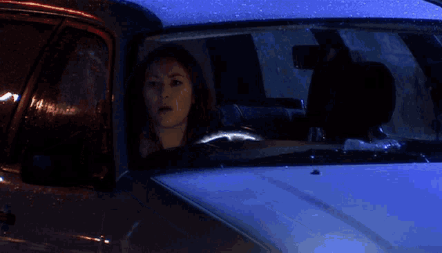 a woman is driving a car at night and looking out the window with a surprised look on her face