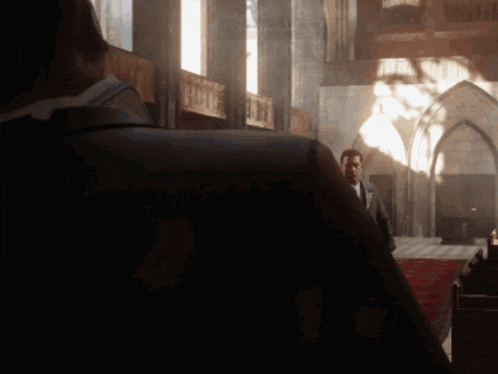 a man in a suit stands in a dark room with arched windows