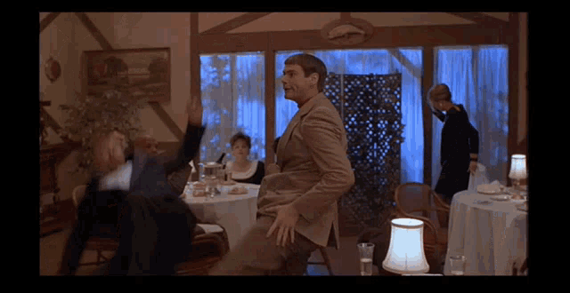 a man in a suit is dancing in a room with tables and a lamp