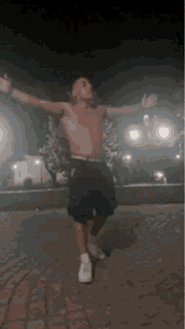 a shirtless man is standing on a brick pavement with his arms outstretched .