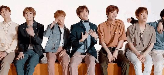 a group of young men are sitting next to each other on a ledge and smiling .