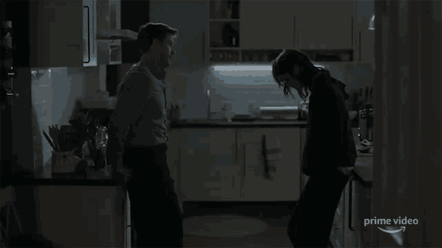 a man and a woman are standing in a dark kitchen with the words prime video on the bottom right