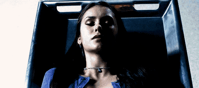 a woman in a blue shirt is laying on a stretcher in a dark room