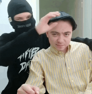 a man wearing a black mask is putting a hat on another man wearing a yellow striped shirt .