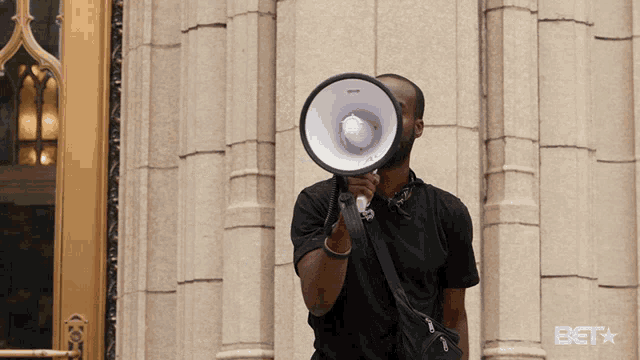 a man is holding a megaphone in front of a building with the bet logo on the bottom