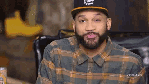 a man with a beard wearing a plaid shirt and a viceland hat