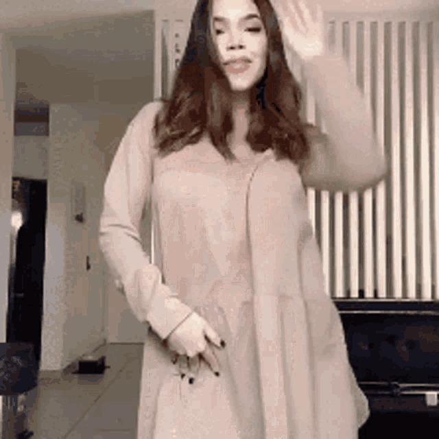 a woman in a beige dress is dancing in a room