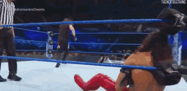 a wrestler is laying on the floor in a wrestling ring while a referee stands behind him .