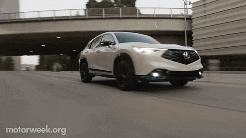a white car is driving under a bridge with a motorweek.org logo in the corner