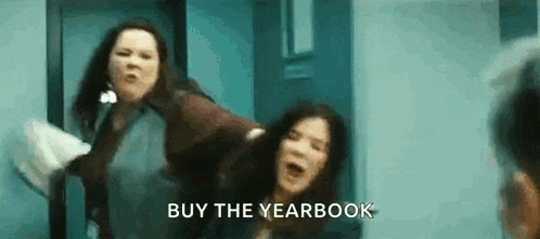 two women are fighting in a hallway with the words `` buy the yearbook '' written on the bottom .