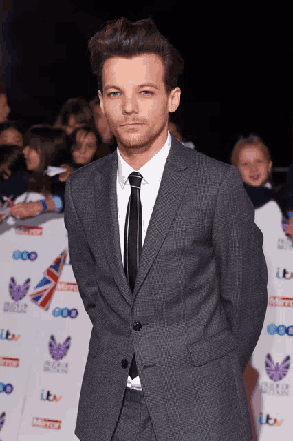 a man in a suit and tie stands in front of a wall that says itv on it