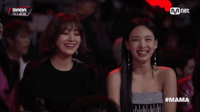 two women are laughing in front of a mnet banner