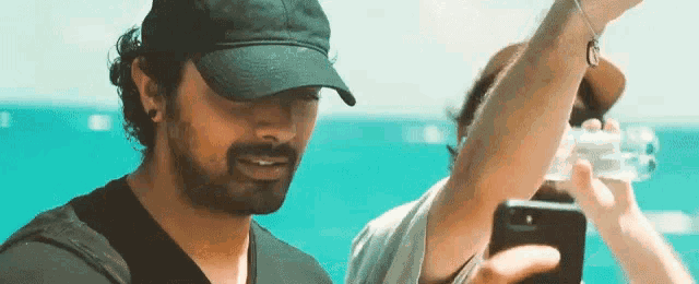 a man wearing a hat is taking a picture of himself with a cell phone .