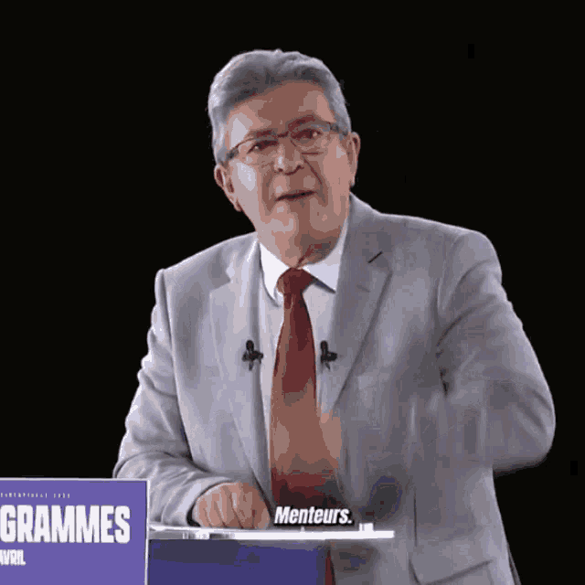a man in a suit and tie stands in front of a sign that says " grammes "