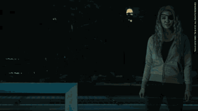 a woman wearing a gray sweater and black pants stands in a dark room