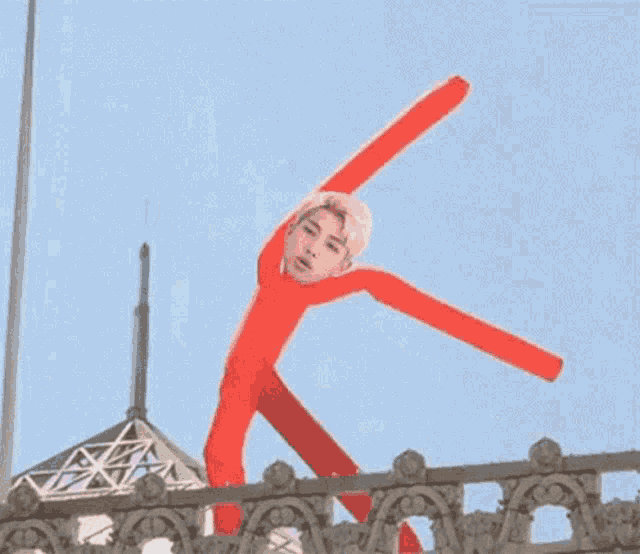 a red inflatable man with a face on it is doing a handstand on a railing .
