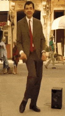 a man in a suit and tie is dancing on a sidewalk in front of a speaker .