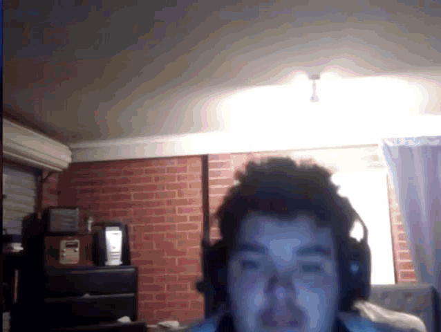 a man wearing headphones looks at the camera with a brick wall in the background
