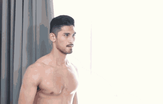 a shirtless man is holding a dumbbell in his hand while standing in front of a window .