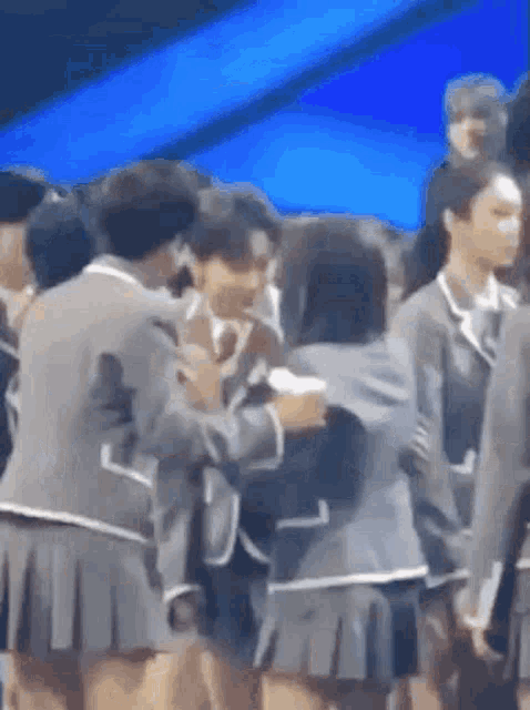 a group of people in school uniforms are hugging each other in a crowd .