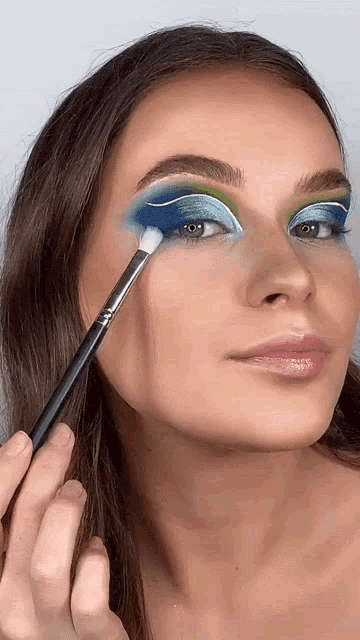 a woman is applying eye shadow with a brush to her eye .