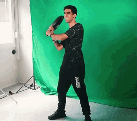 a man is standing in front of a green screen holding a racket and smiling .