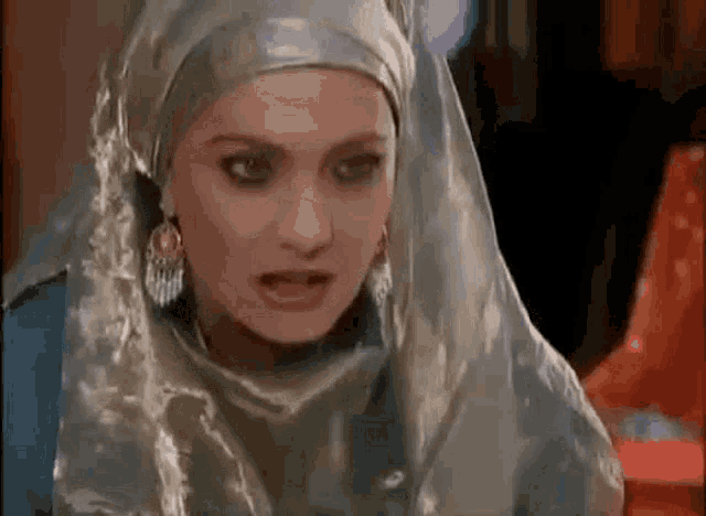 a woman wearing a hijab and earrings is looking at the camera .