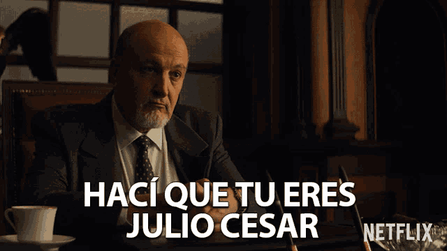 a man in a suit and tie is sitting at a desk with the words " haci que tu eres julio cesar " written above him