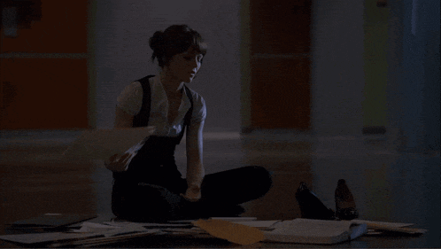 a woman is sitting on the floor with a pile of papers on the floor